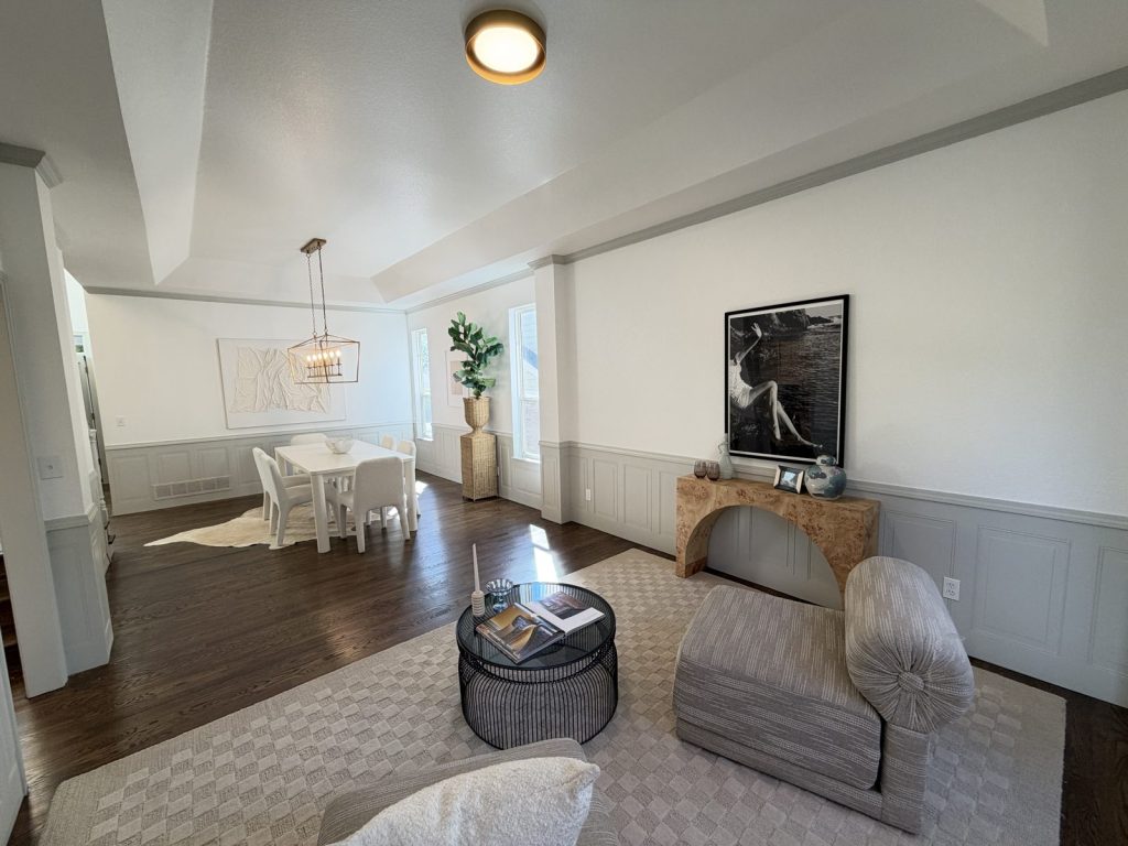 Living and dining room after the remodel in Highlands Ranch, with dark hardwood floors, painted wainscoting panels, and new light fixtures under the tray ceiling