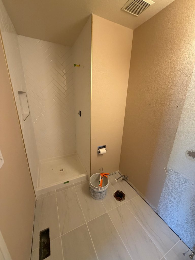 Bathroom with white herringbone tile shower walls, a tiled niche, and large gray floor tile installed, before fixtures and final paint