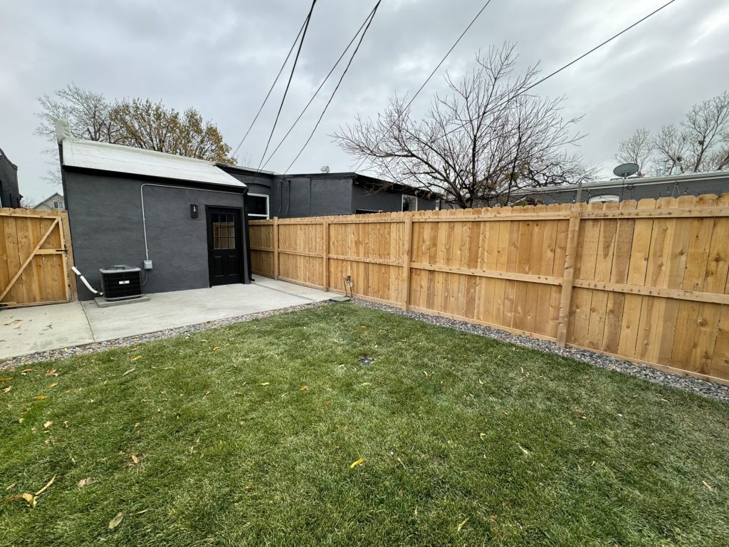 Backyard with a new cedar privacy fence and gate, concrete patio, gravel border, fresh lawn, and dark-painted exterior walls