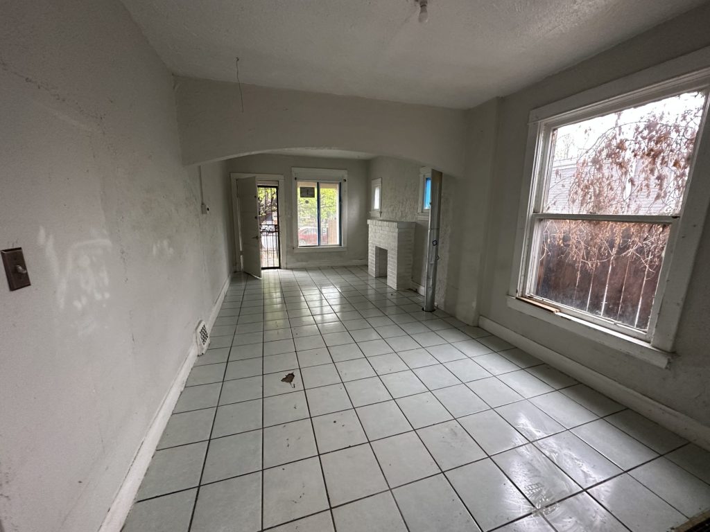 Living room before remodeling with white ceramic floor tile, stained walls, an arched opening, and a painted brick fireplace